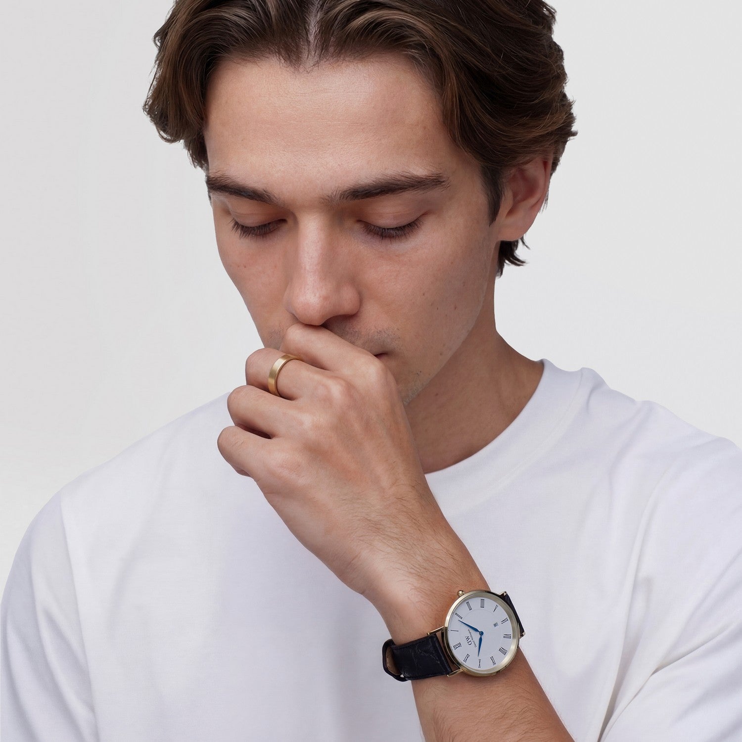 Man wearing a white t-shirt and a watch, looking down.