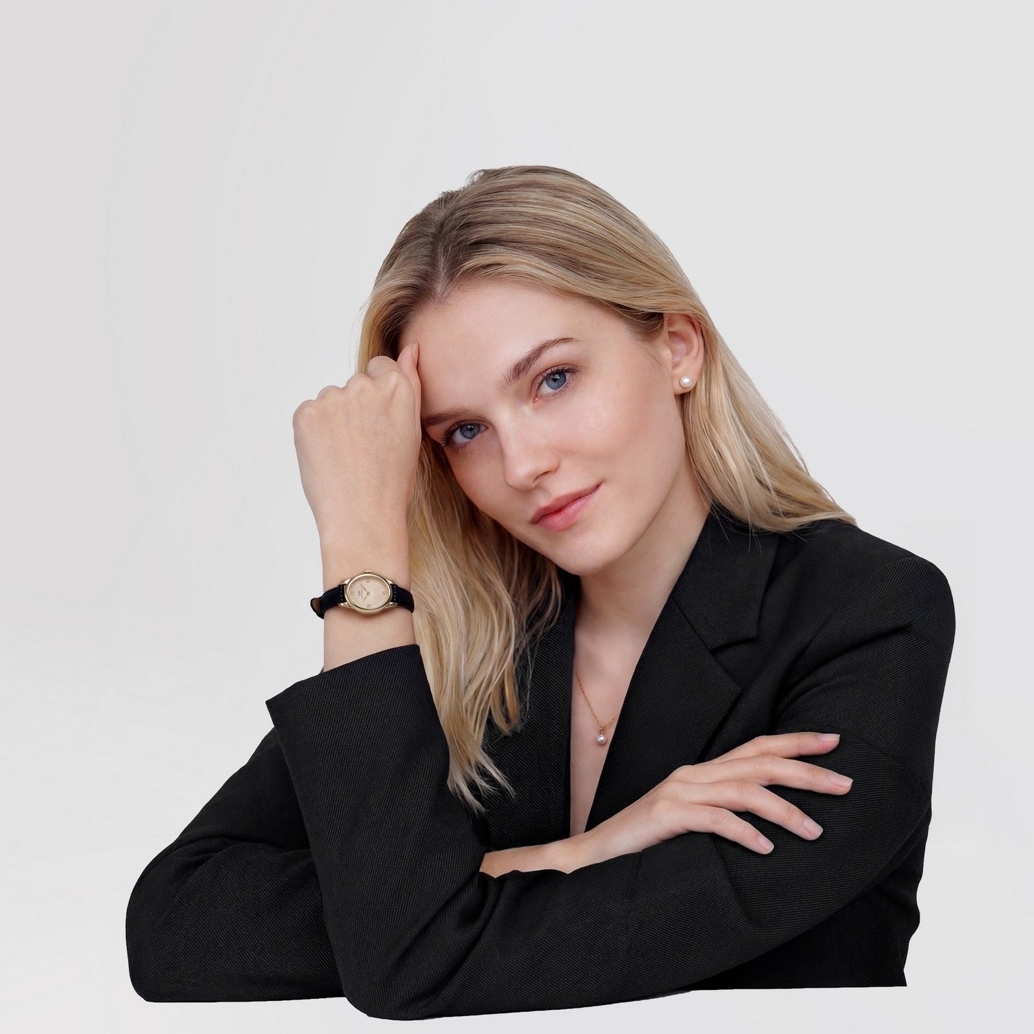 Woman wearing a black blazer and a watch on a plain background