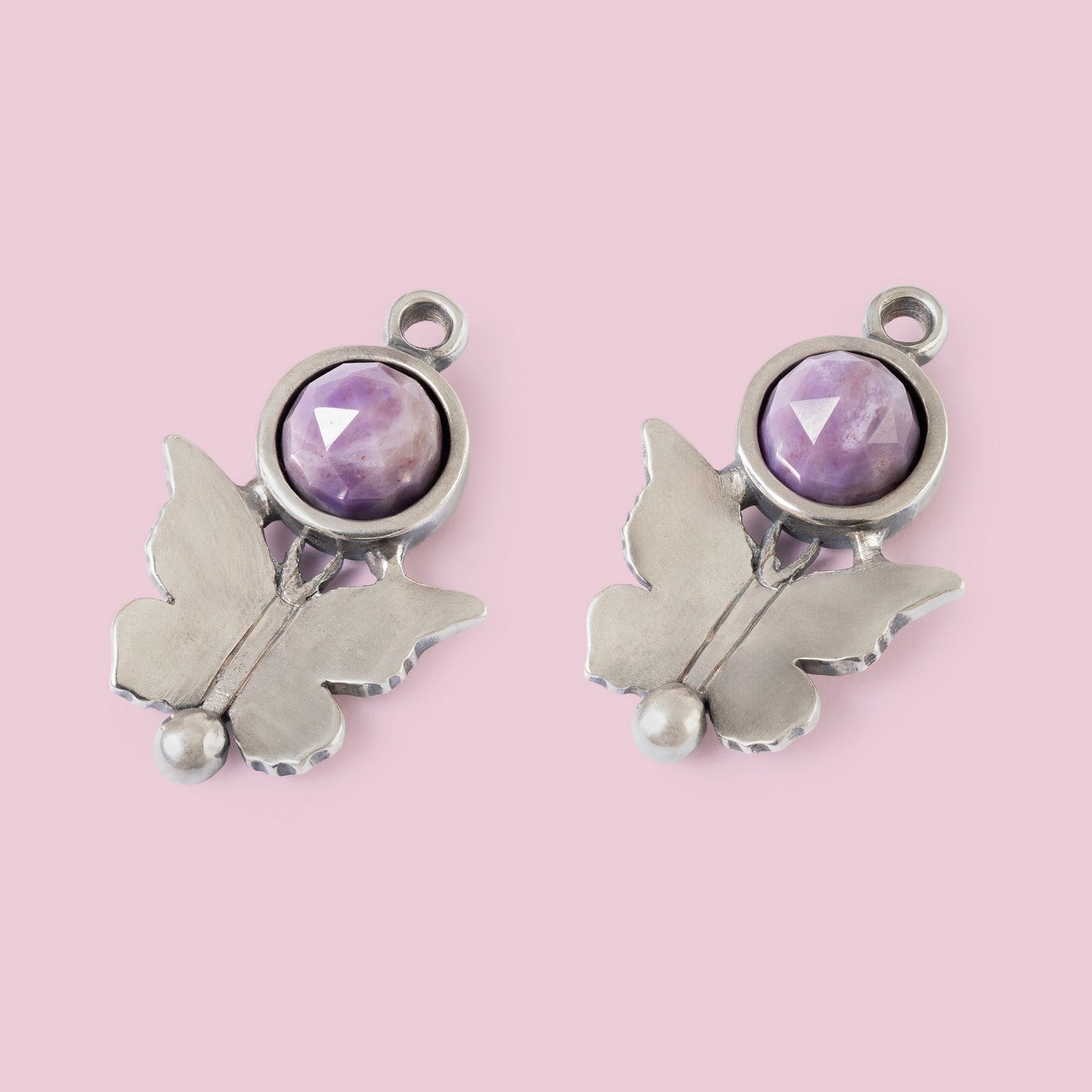 Butterfly-shaped charms with purple gemstones on a pink background