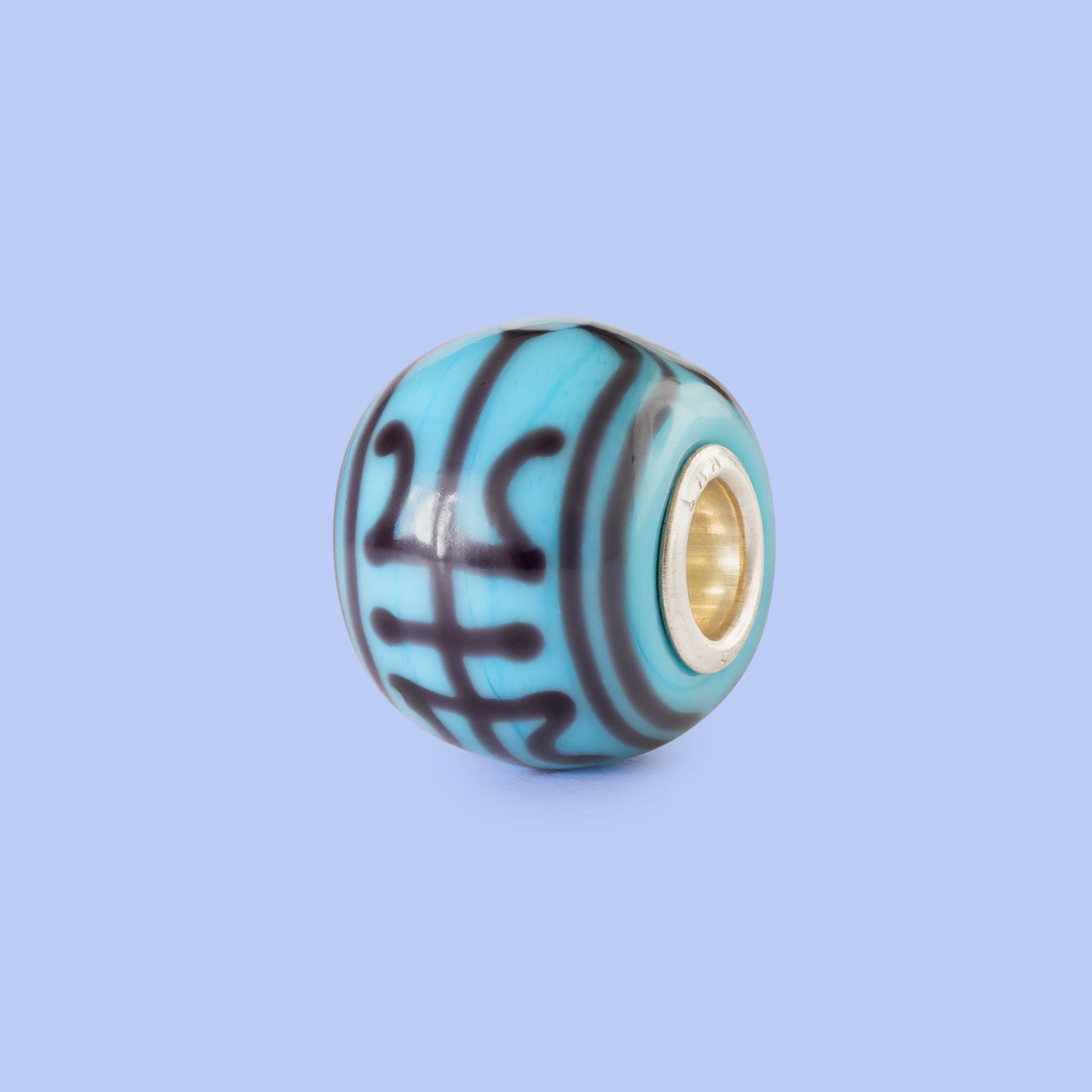 Turquoise glass charm with gold core on a light blue background