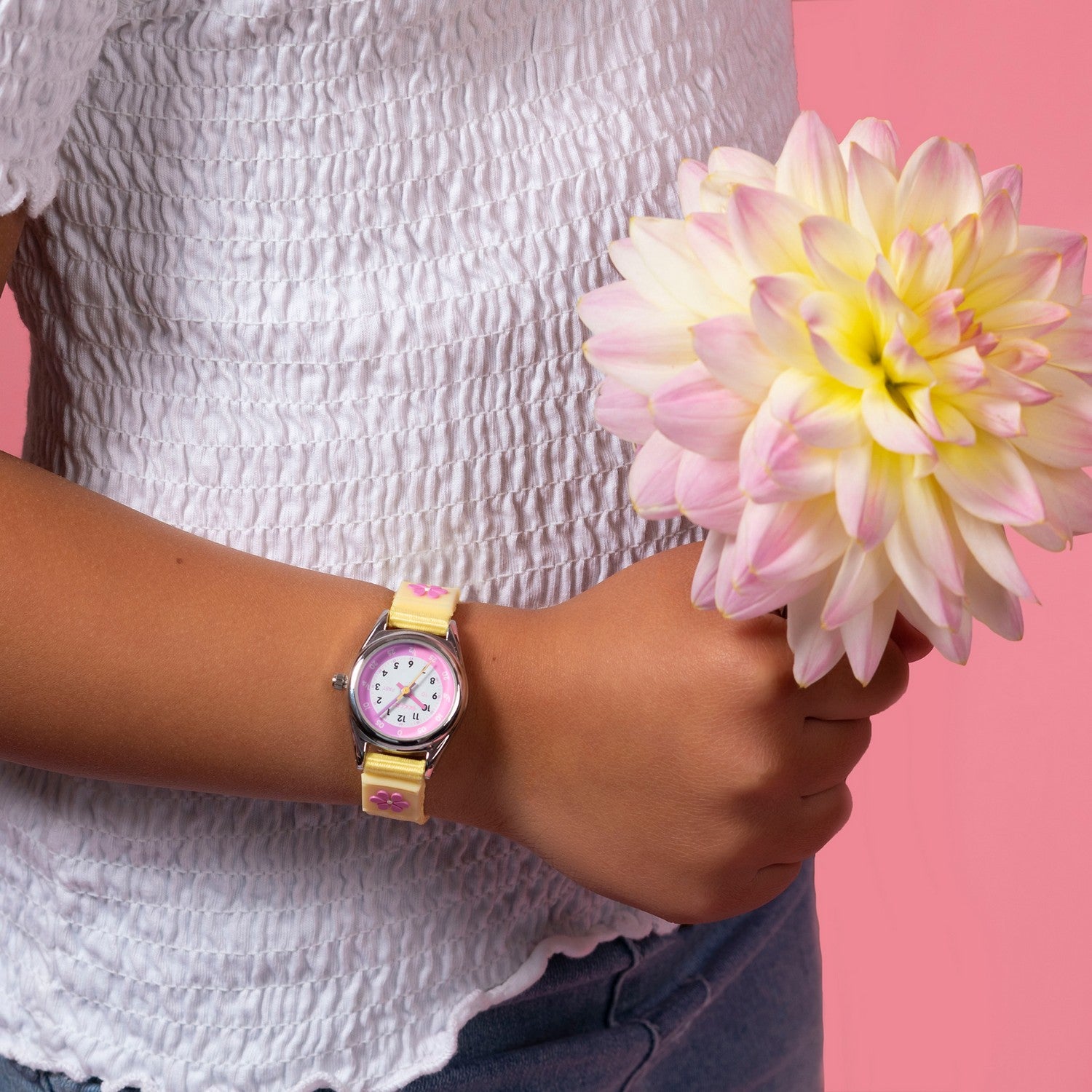 Person wearing a watch with a pink flower against a pink background