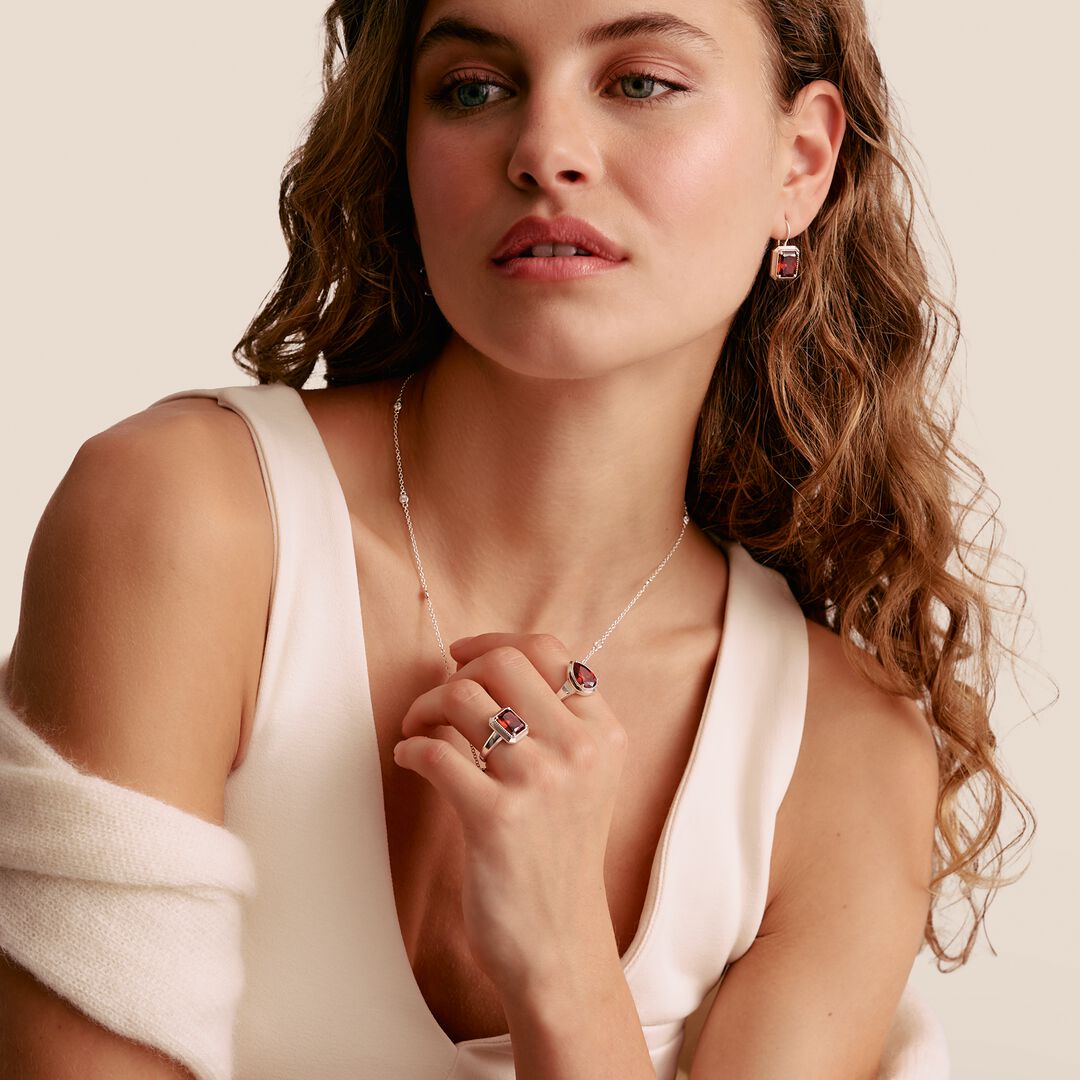 Woman wearing jewelry including a necklace, ring, and earrings on a neutral background