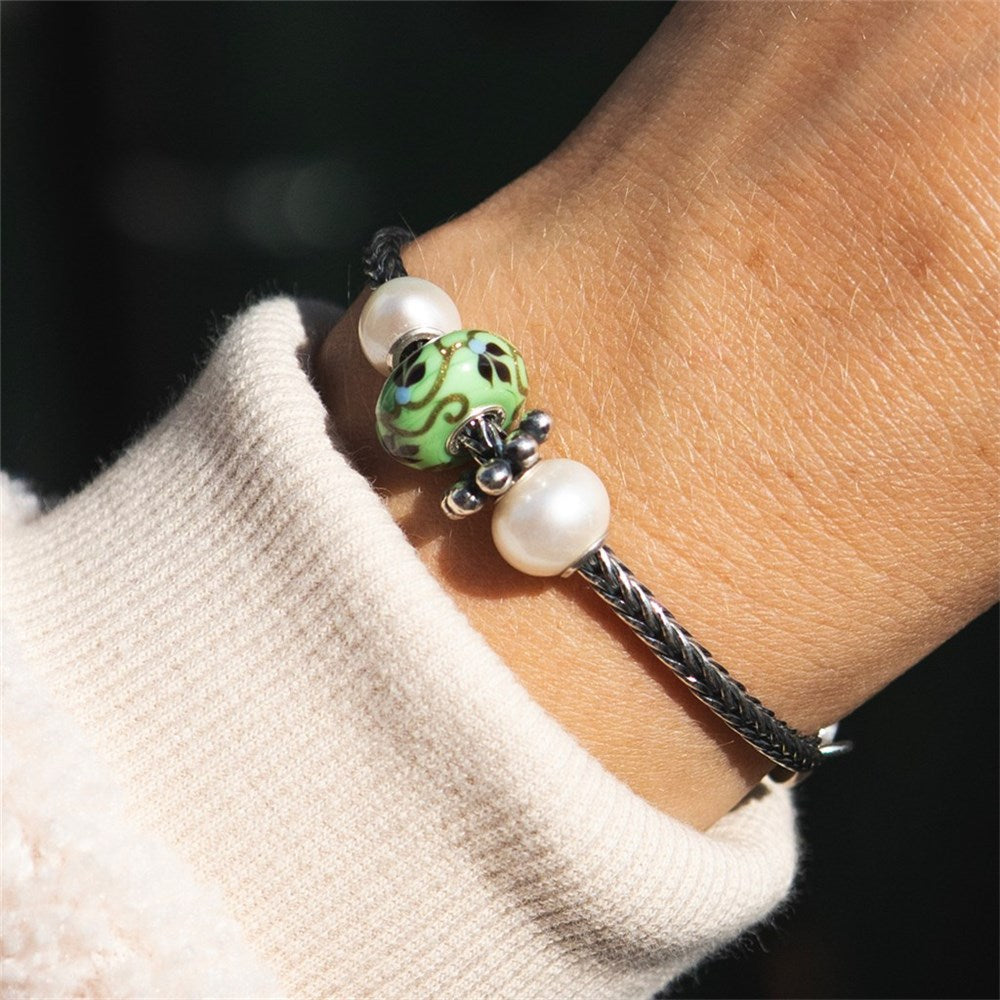 Bracelet with green and white beads on a wrist wearing a beige sweater.