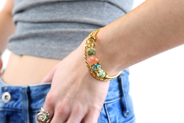 Close-up of a hand wearing a gold bracelet with colorful beads on a blurred background
