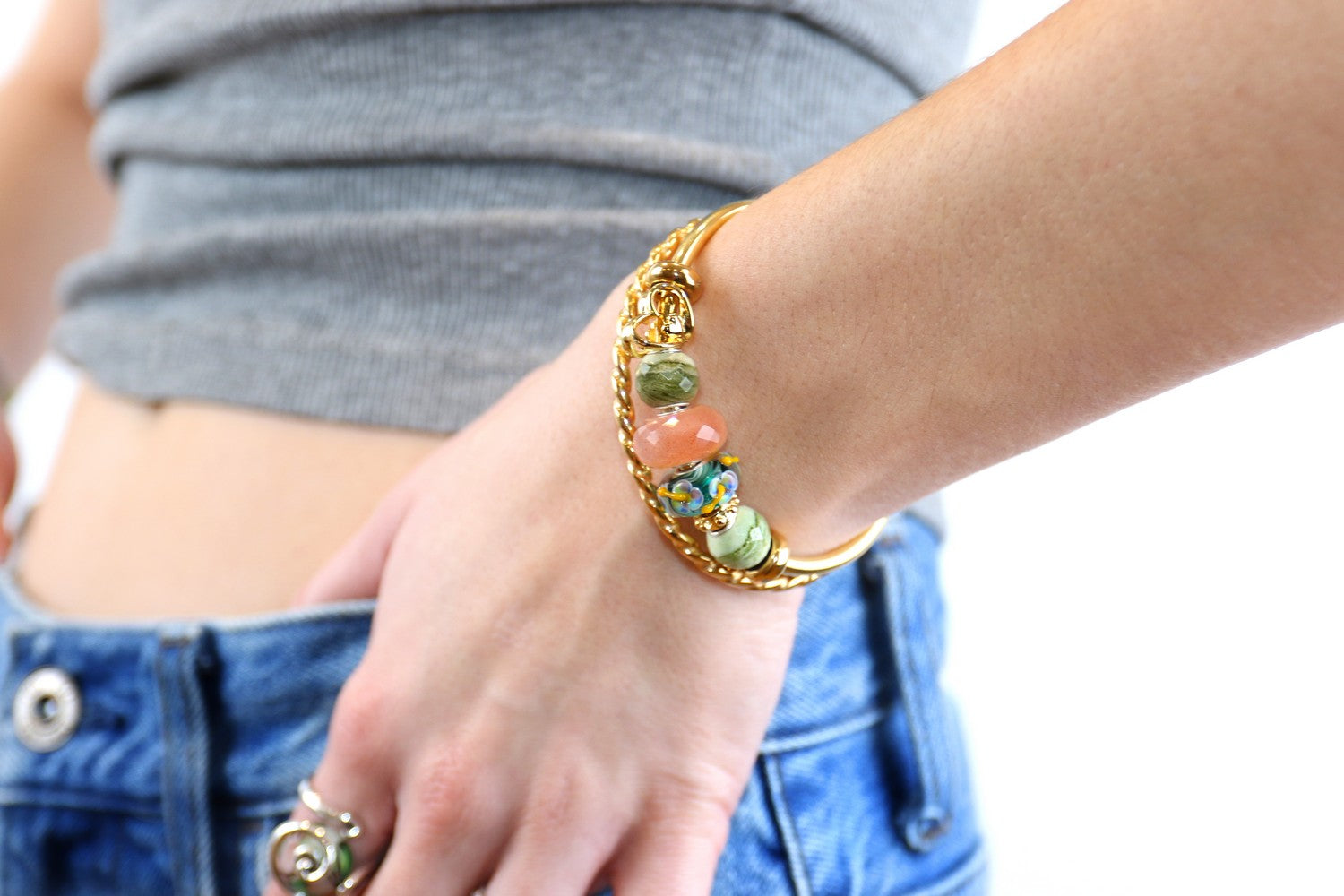 Close-up of a hand wearing a gold bracelet with colorful beads on a blurred background
