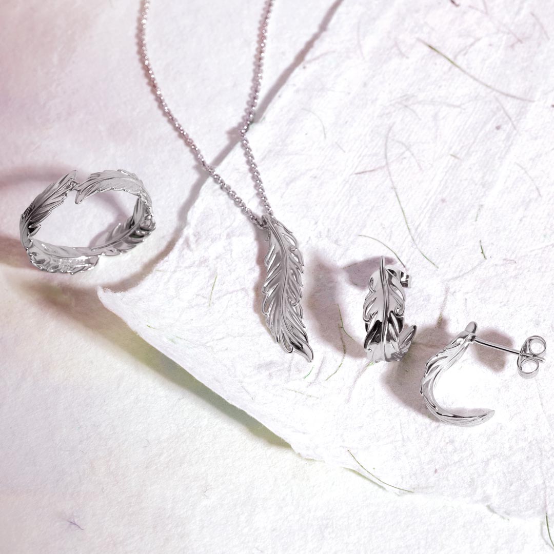 Silver jewelry set including a ring, necklace, and earrings on a textured white surface.