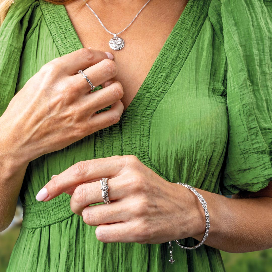 Person wearing a green dress with jewelry including rings and a necklace.