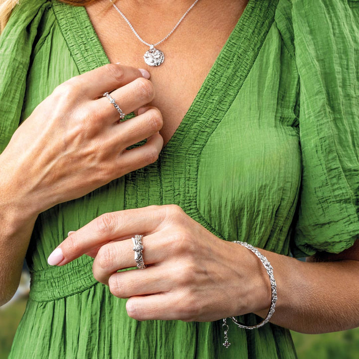 Person wearing a green dress with jewelry including rings and a necklace.
