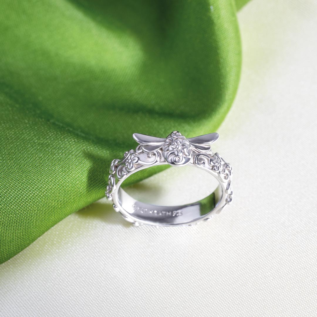 Silver ring with intricate design on a green and white fabric background