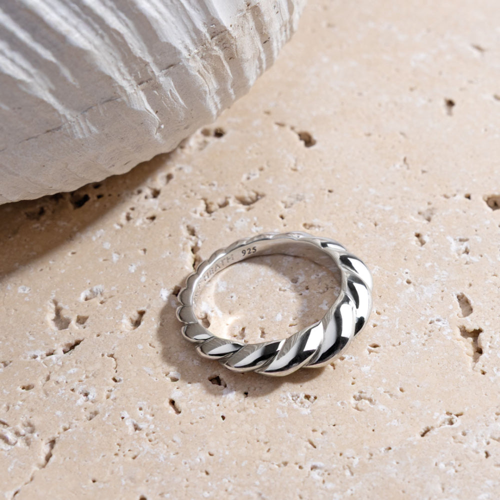 Silver ring with a twisted design on a sandy surface