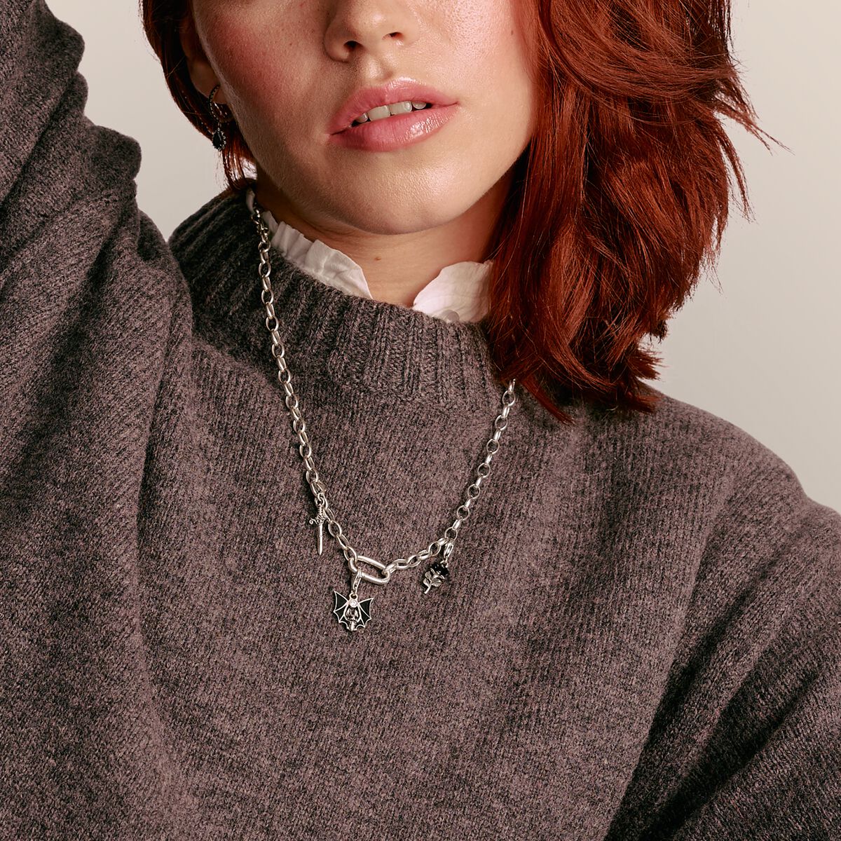 Person wearing a silver necklace with a pendant against a neutral background