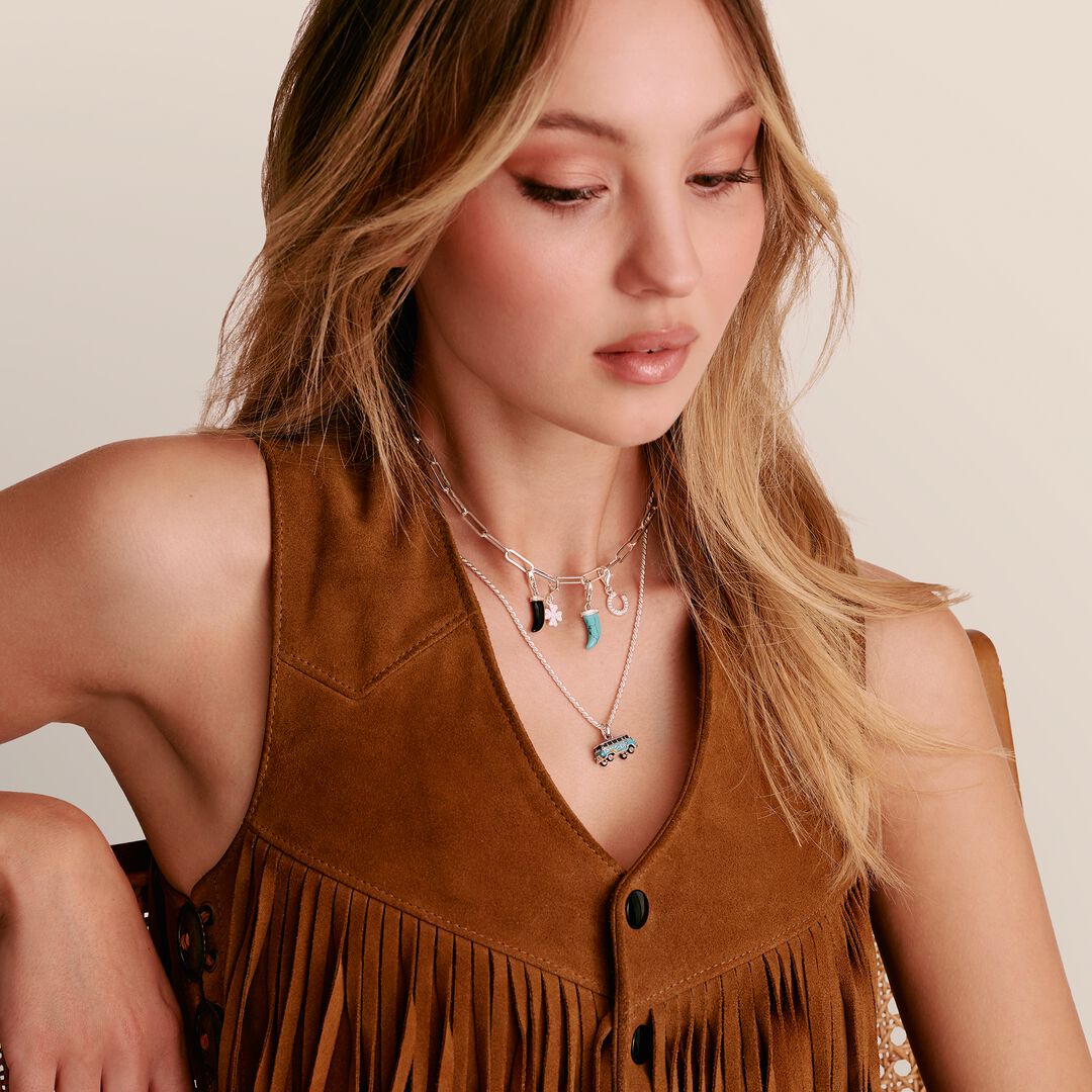 Woman wearing a brown suede vest with fringe details and layered necklaces.