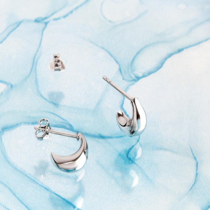 Silver moon-shaped earrings on a light blue marble background