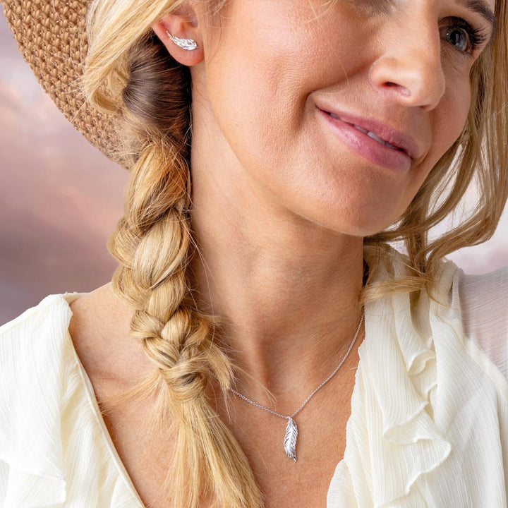 Woman with braided hair wearing a straw hat and a necklace with a feather pendant.