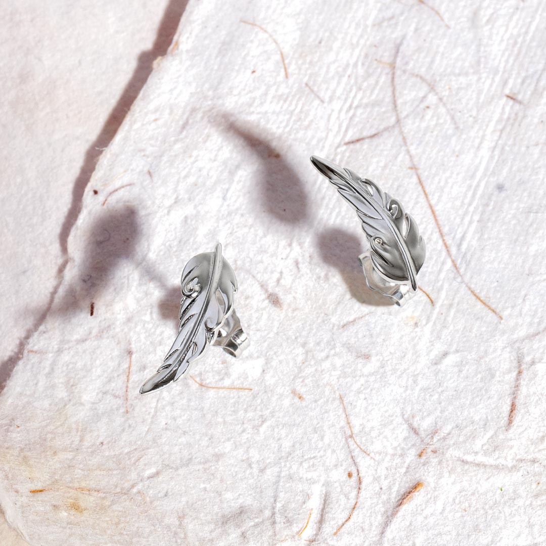 Silver feather-shaped earrings on a textured white surface