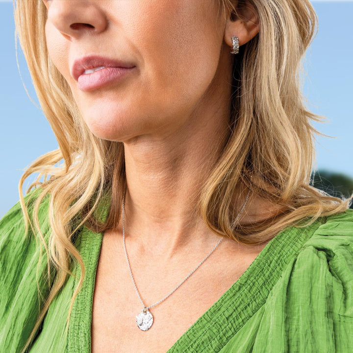 Close-up of a woman wearing a green top with a necklace and earrings against a blue background