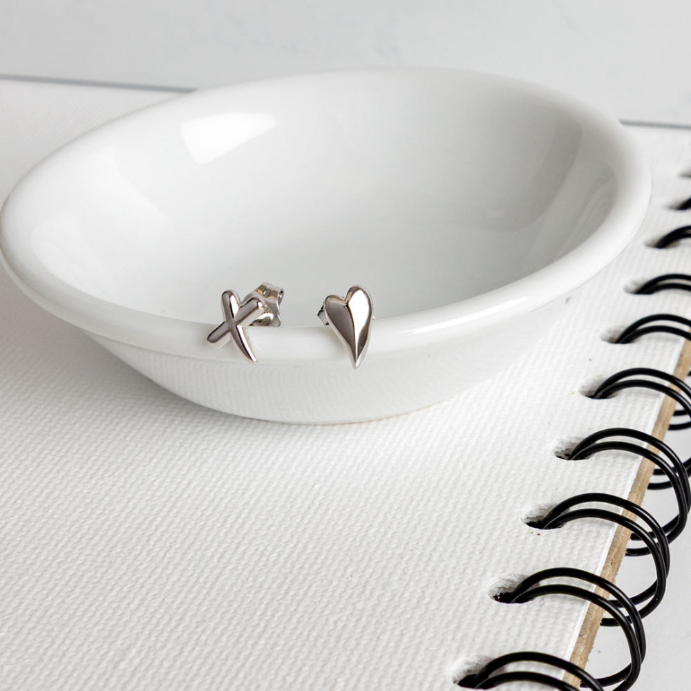 Silver earrings on a white dish with a notebook in the background