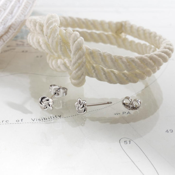 White rope-style headband and silver knot earrings on a white surface