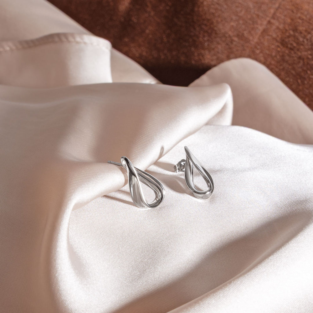 Silver earrings on a soft pink fabric background