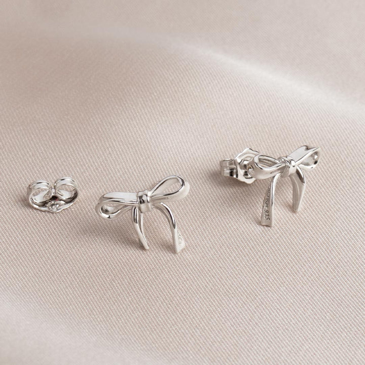 Set of silver bow-shaped earrings on a light beige fabric background