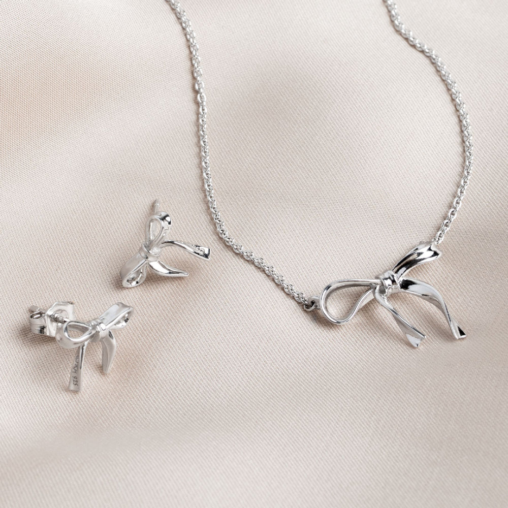 Silver bow-shaped necklace and earrings on a light pink background