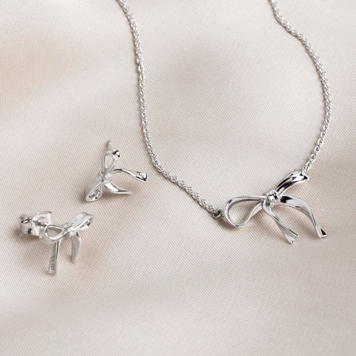 Silver bow-shaped necklace and earrings on a light pink background