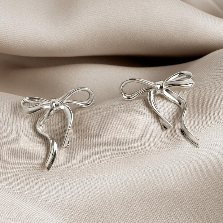 Silver bow-shaped earrings on a beige fabric background