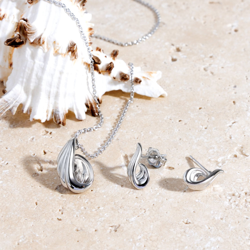 Silver jewelry set including necklace, earrings, andpendant on sand with shells.