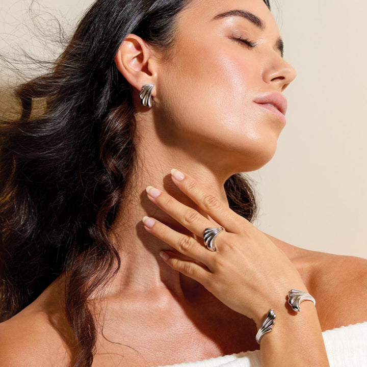 Woman wearing silver earrings, ring, and bracelet against a beige background
