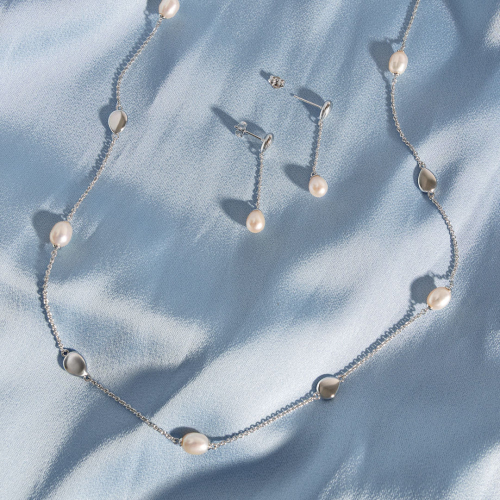 Pearl necklace and earrings on a light blue fabric background