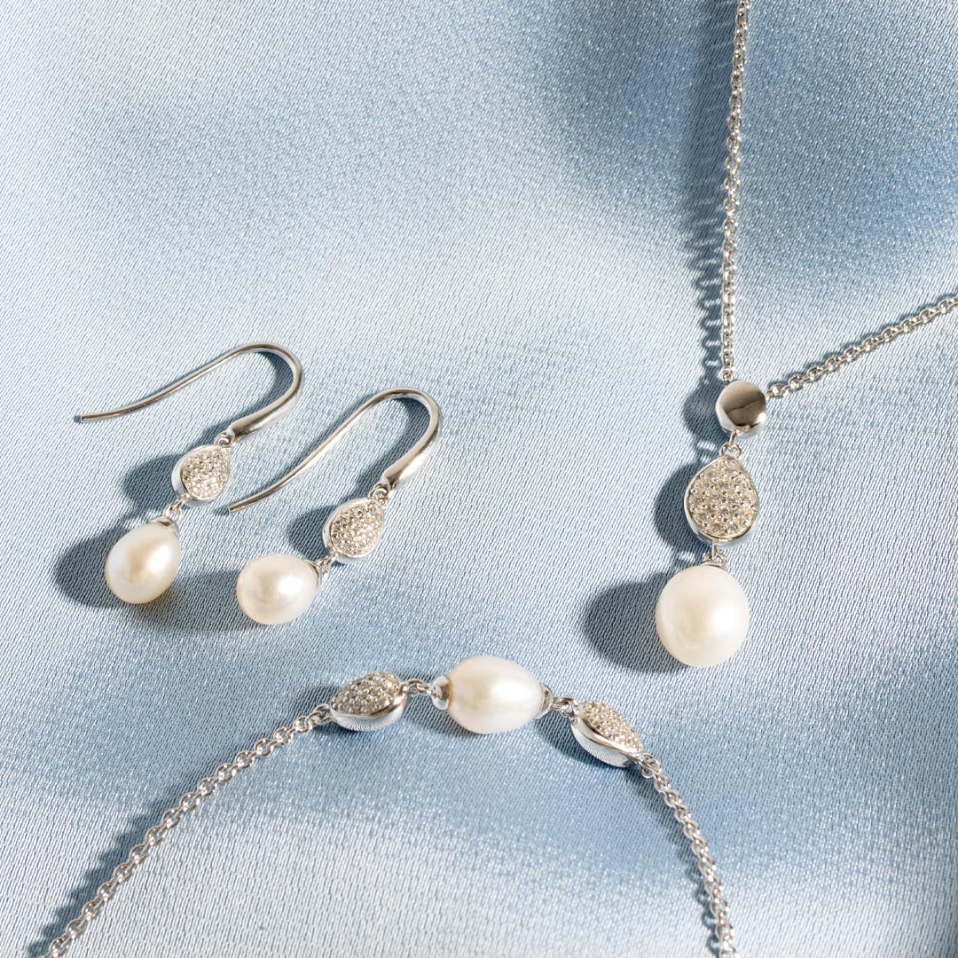 Pearl necklace and earrings on a light blue fabric background