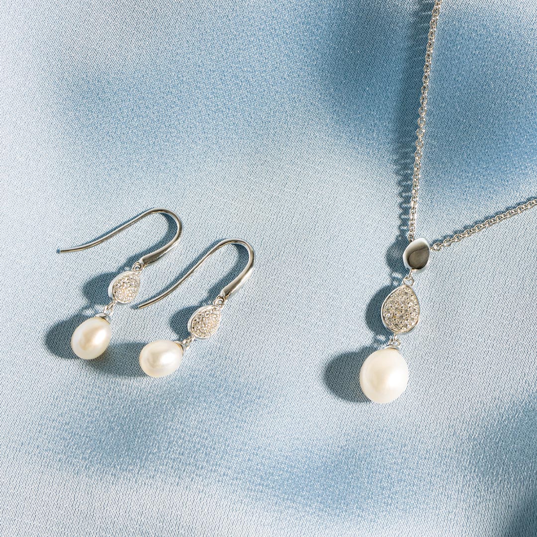 Pearl earrings and necklace on a light blue fabric background