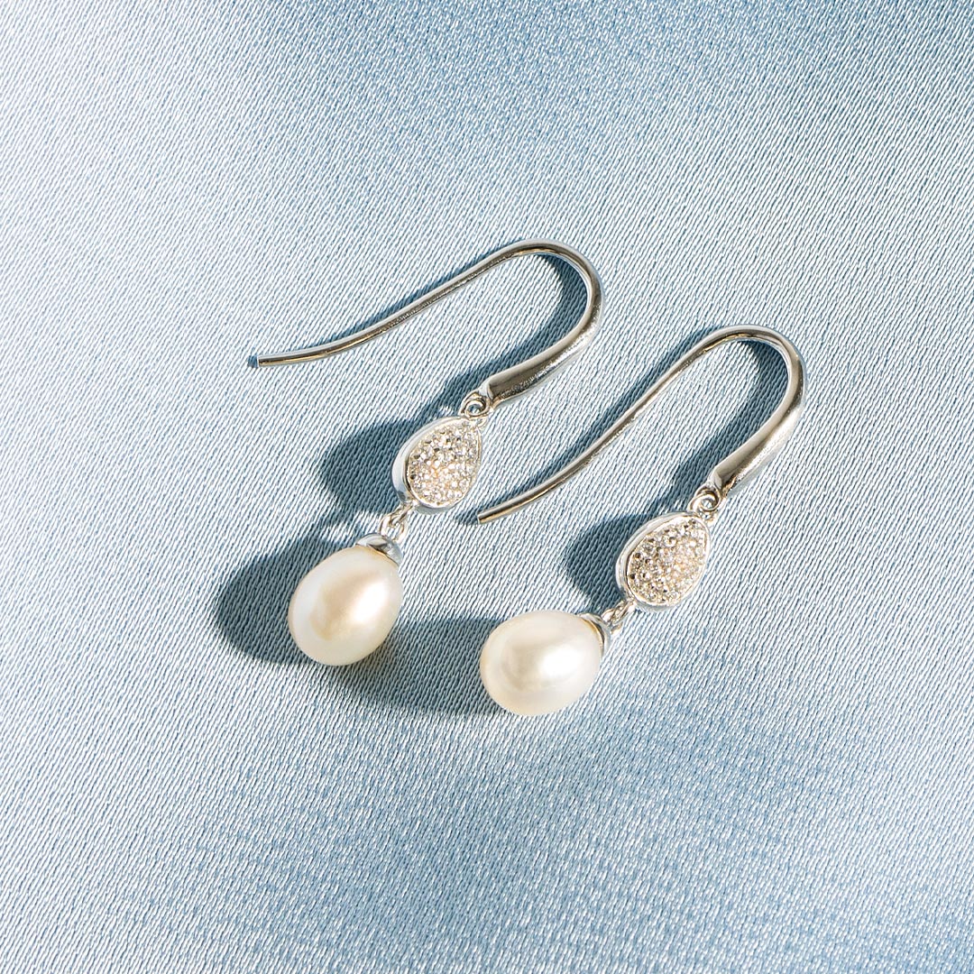 Pearl earrings with silver hooks on a light blue fabric background