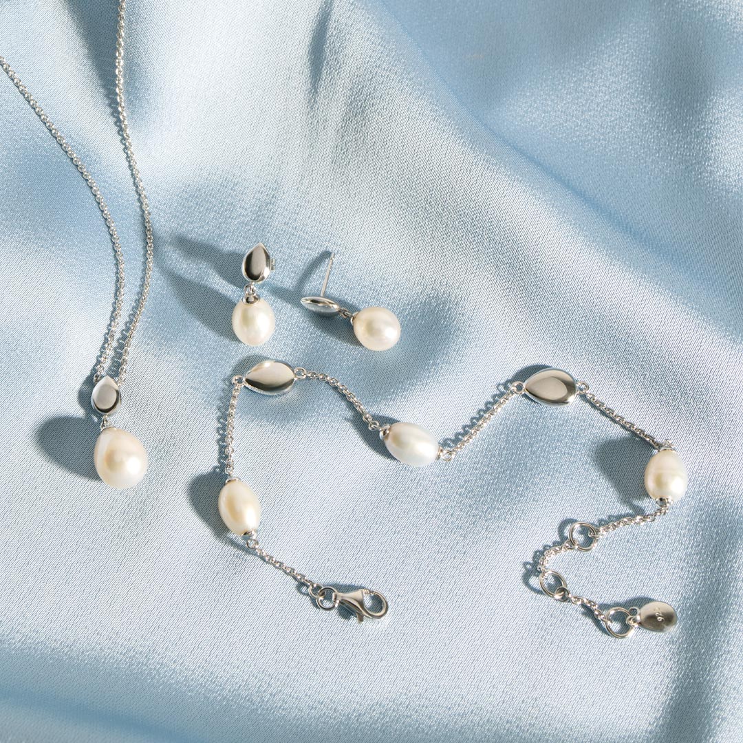Pearl necklace, earrings, and bracelet on a light blue fabric background