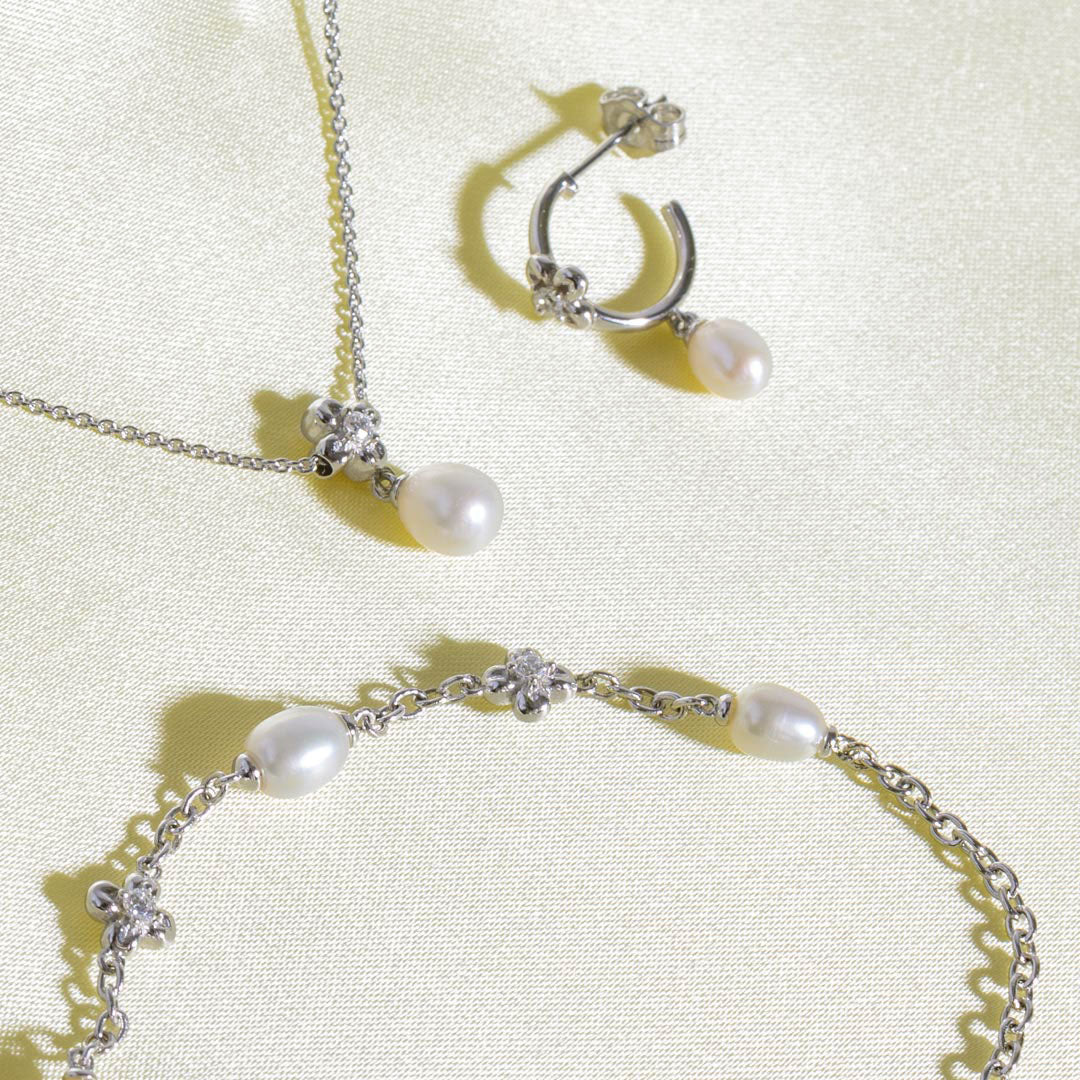 Pearl necklace, earrings, and bracelet set on a light background