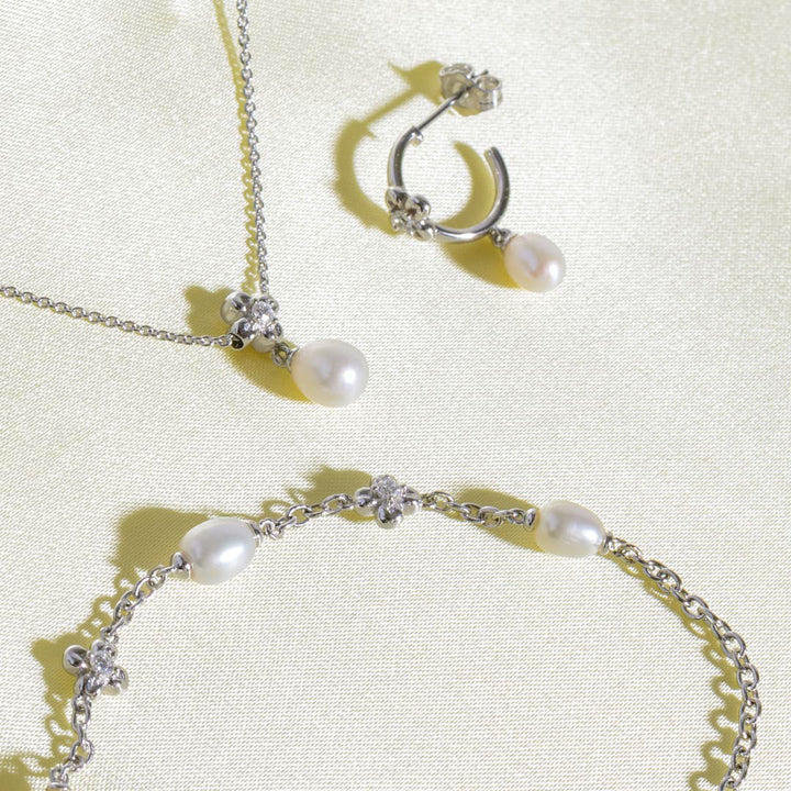 Pearl necklace, earrings, and bracelet set on a light background