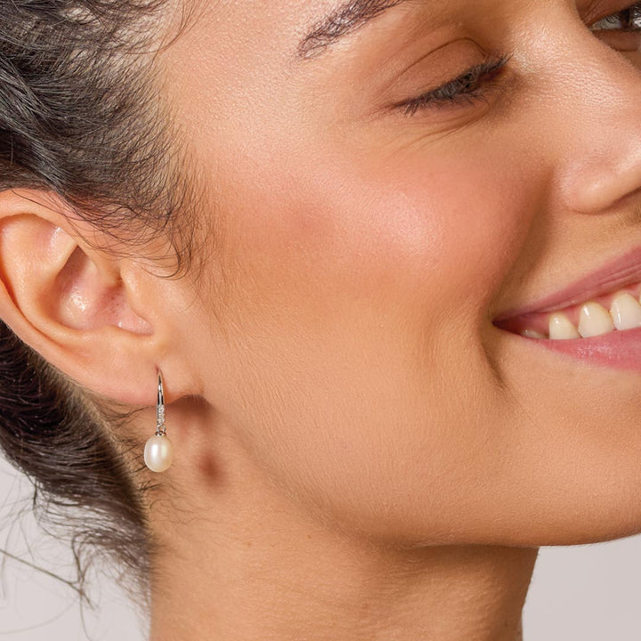 Close-up of a woman wearing pearl earrings with a neutral background