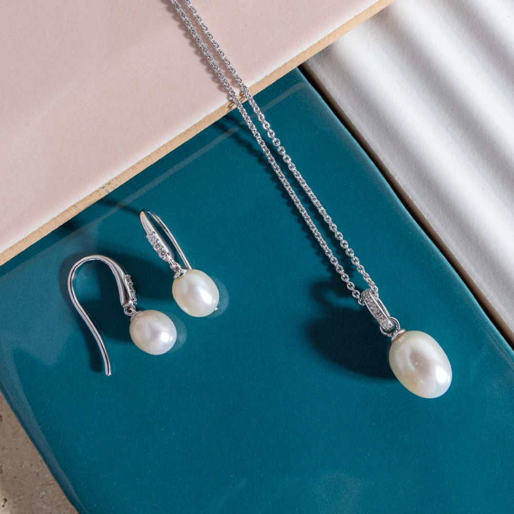 Pearl earrings and necklace on a teal surface