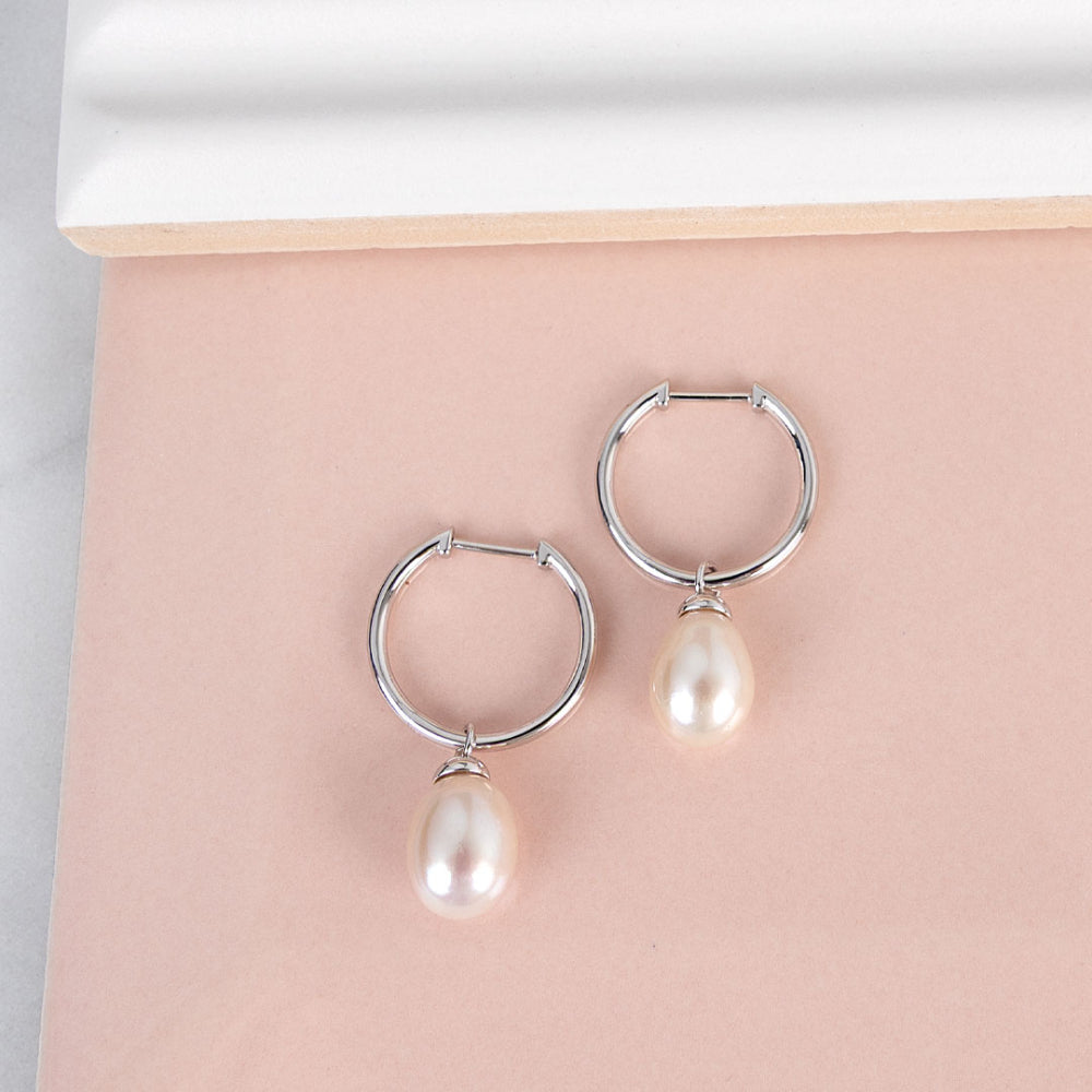 Silver hoop earrings with pearl drops on a pink surface