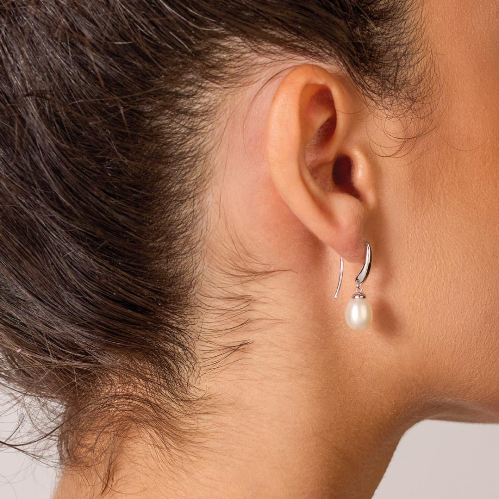 Close-up of an ear wearing a pearl earring with a neutral background