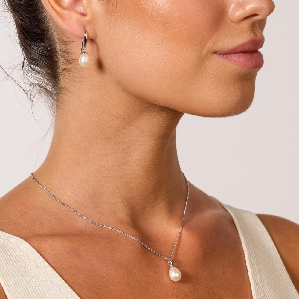 Close-up of a woman wearing a pearl necklace and earrings on a neutral background