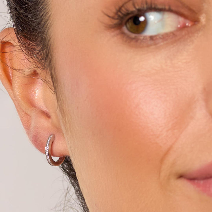 Close-up of a woman's ear wearing a silver hoop earring with a neutral background