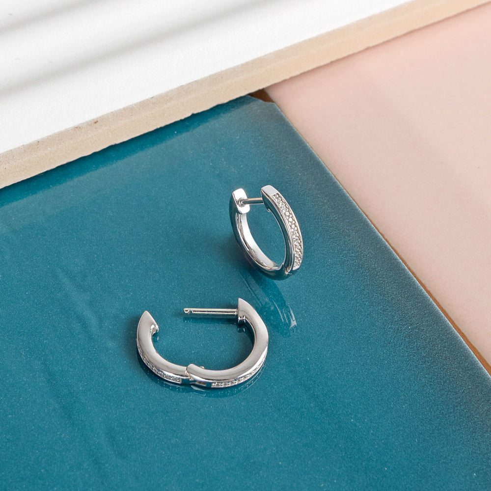 Silver hoop earrings on a teal surface with a light wood frame.