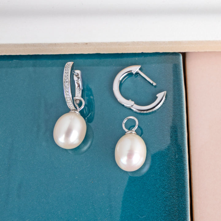 Pearl earrings with silver hooks on a teal surface