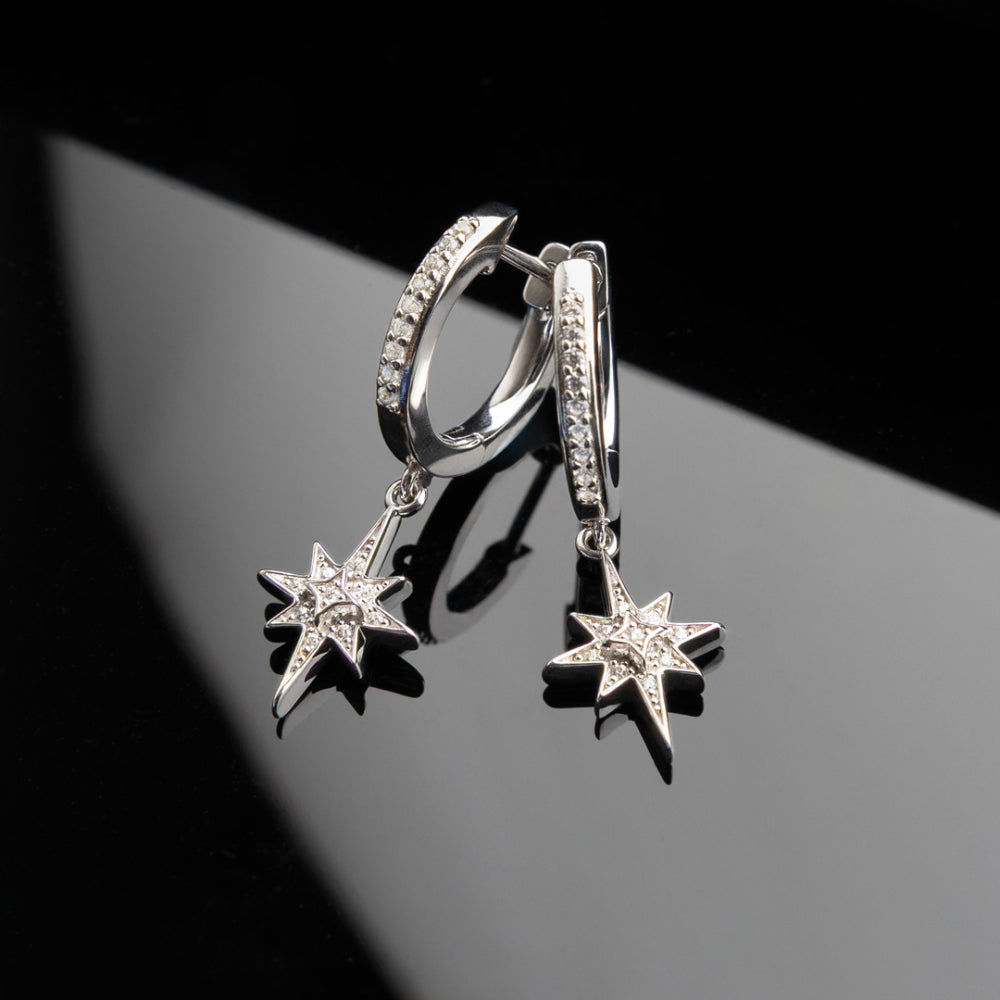 Silver hoop earrings with star-shaped charms on a reflective surface