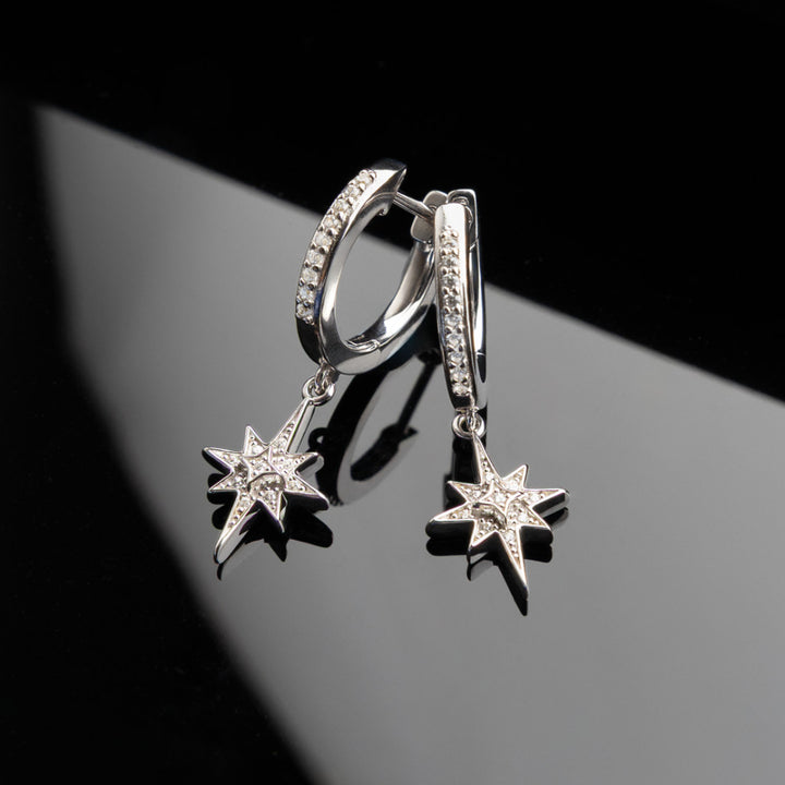 Silver hoop earrings with star-shaped charms on a reflective surface