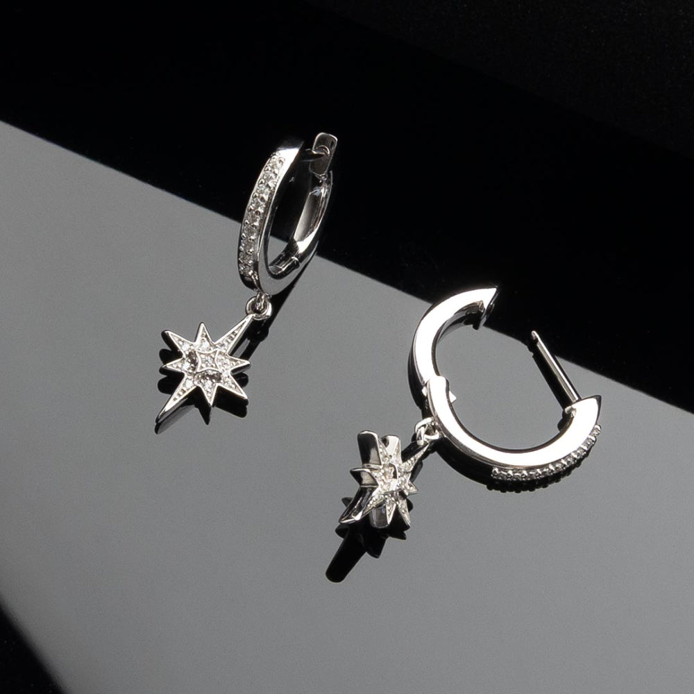 Silver hoop earrings with star and moon charms on a black and gray gradient background