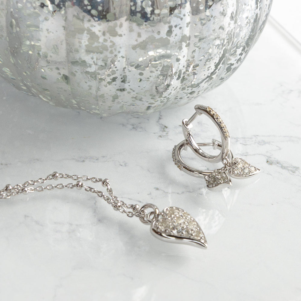 Silver heart-shaped jewelry set on a marble surface with a textured silver bowl in the background.