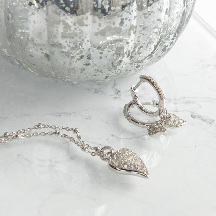 Silver heart-shaped jewelry set on a marble surface with a textured silver bowl in the background.