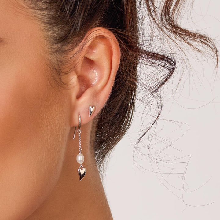 Close-up of a woman's ear wearing a silver earring with a heart and pearl design.